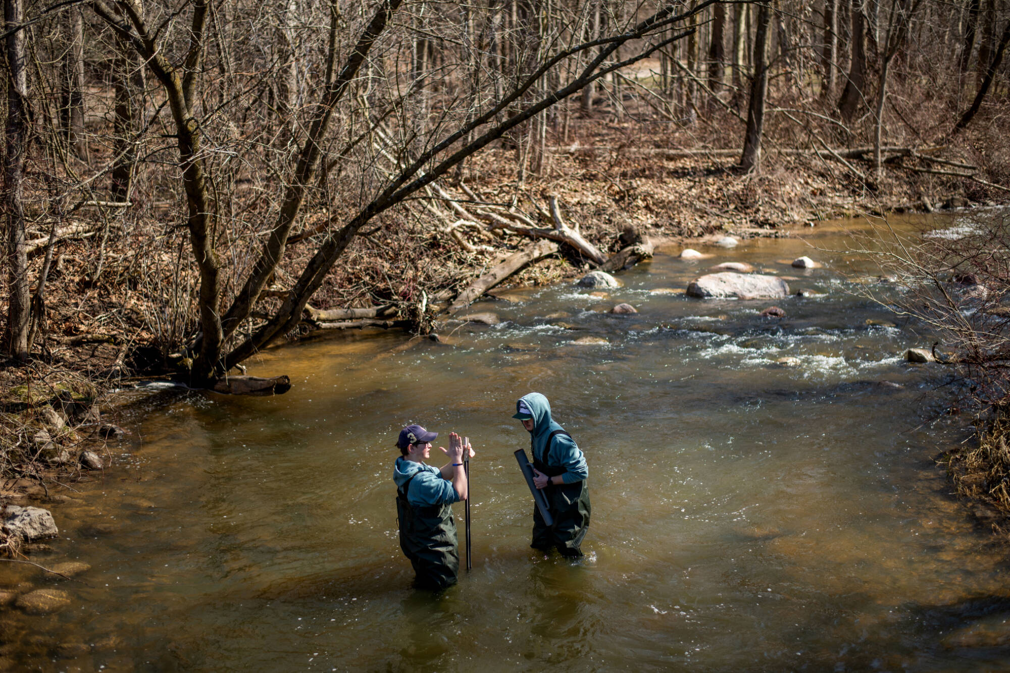 Two students standing in the middle of a stream place working on installing a pole